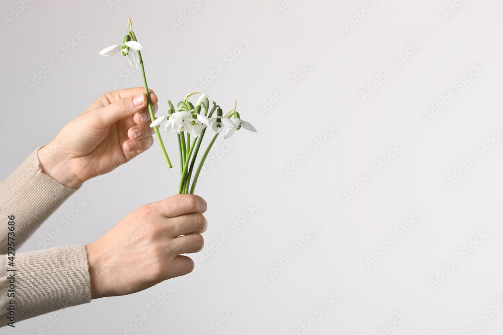 Woman holding beautiful bouquet of snowdrops on light background, closeup. Space for text