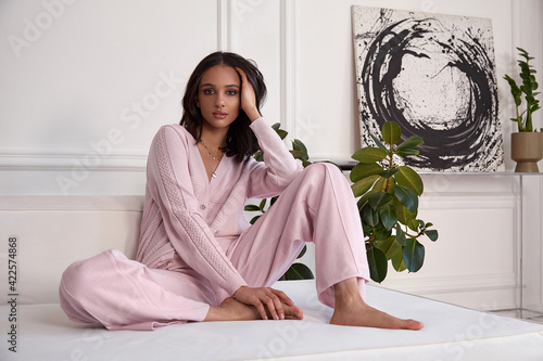 Pretty fashion beautiful woman sexy lady brunette curly hair dark tanned skin wear trend clothes knitted pink pink suit jacket top pants shoes interior room sofa plants spring collection luxury life.