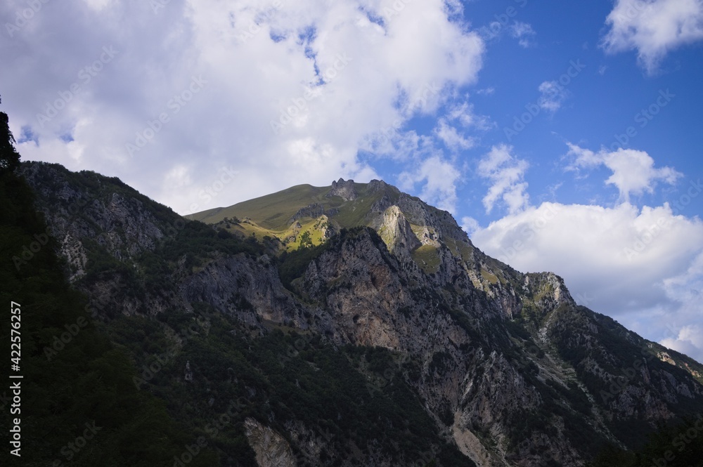 Fototapeta premium The top of a rocky mountain with green meadows illuminated by a beam of light (Sibillini National Park, Marche, Italy)