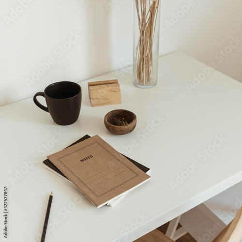 Women's home office workspace. Freelance work, business workplace. Light aesthetic hygge space with wooden chair, table, reed pampas grass bouquet, mug, notebook. Modern interior design. photo