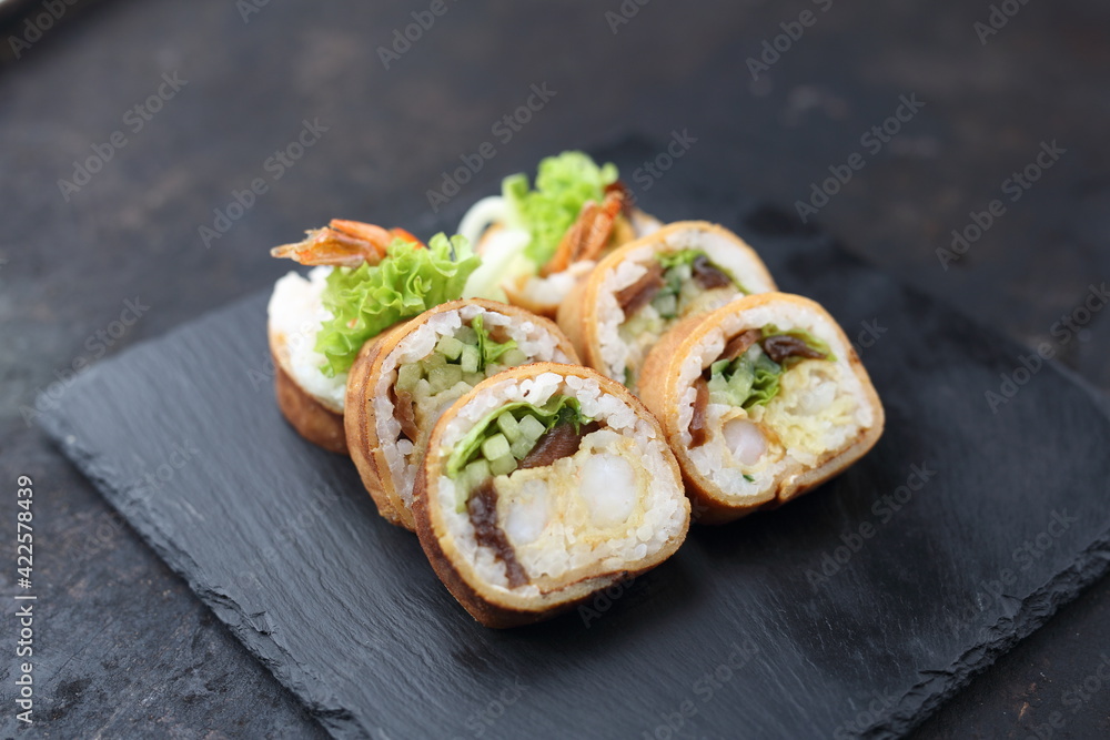 Tempura maki rolls with shrimp, lettuce, cucumber and pickled radish. 6 piece sushi set in Japanese omelette, on a black stony background. Japanese cuisine delicacy. Tempura maki rolls with shrimp, lettuce, cucumber and pickled radish. 6 piece sushi set in Japanese omelette, on a black stony background. Japanese cuisine delicacy.