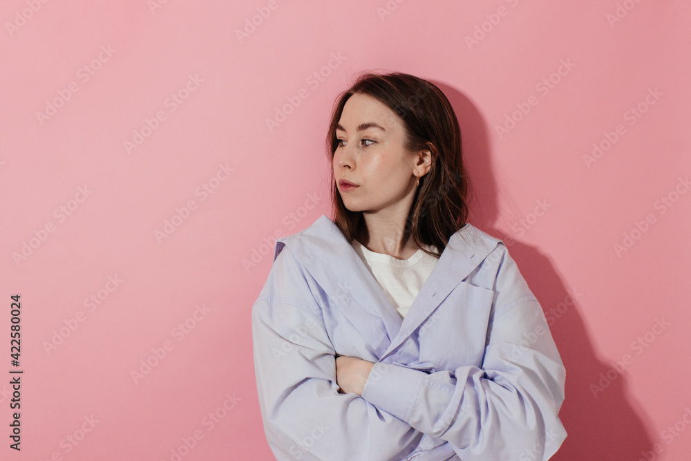 Frustrated young woman in blue shirt with natural makeup standing over pink background arms folded looking to the left side copy space. Confident millennial girl standing alone studio shot. Frustrated young woman in blue shirt with natural makeup standing over pink background arms folded looking to the left side copy space. Confident millennial girl standing alone studio shot.