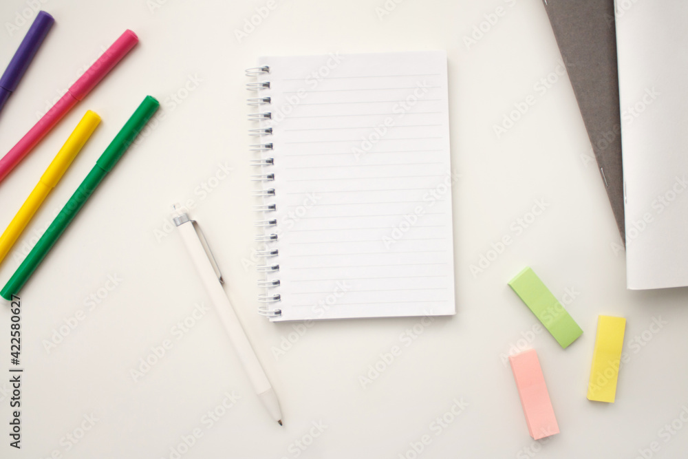 An open notebook on a white background with colored pencils and felt-tip pens, a ruler and scissors. The notebook lies on a plain background with space for writing. Composition of writing to-dos for t An open notebook on a white background with colored pencils and felt-tip pens, a ruler and scissors. The notebook lies on a plain background with space for writing. Composition of writing to-dos for t