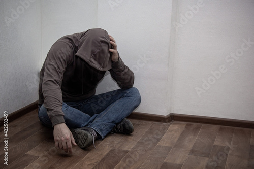 desperate young drug addict wearing hood and sitting alone in corner © dashtik