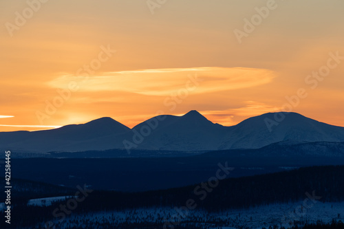 Sunset behind Norwegian mountains in winter. Orange sky and snow covered woodland. Shot in Sweden, Scandinavia