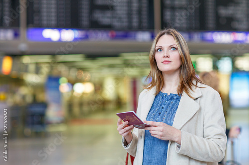 Woman at international airport, checking electronic board and waiting for her flight. Female passenger with european passport at departure terminal, indoors photo