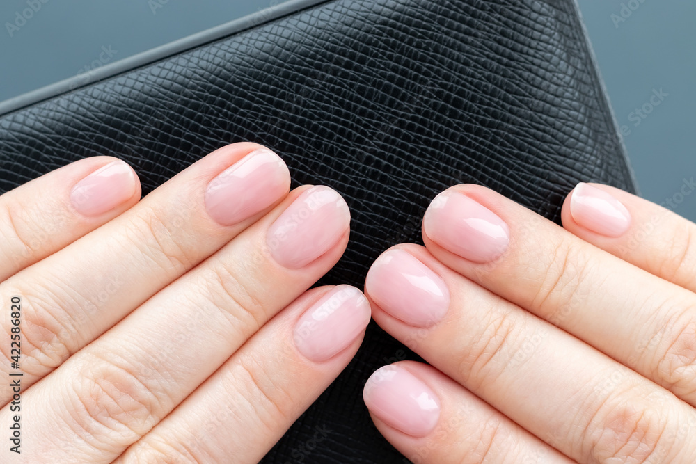 Female hands with beautiful manicure - pink nude nails on black leather surface on gray background. Closeup view