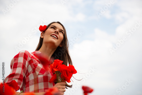 Young beautiful cheerful woman walking among blooming poppy at spring field, summer nature outdoor. photo