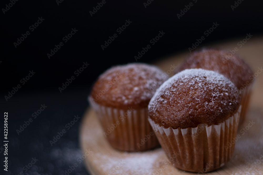 three muffins covered in powdered sugar on wooden stand isolated on black dark background. sweet bakery three muffins covered in powdered sugar on wooden stand isolated on black dark background. sweet bakery