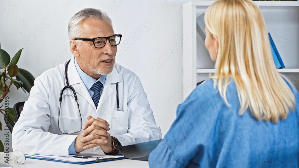 smiling doctor talking to blonde woman during consultation in clinic, blurred foreground smiling doctor talking to blonde woman during consultation in clinic, blurred foreground