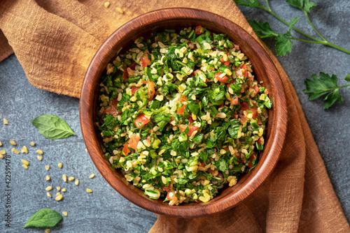 Traditional Arabic salad tabbouleh in a wooden bowl on a dark background top view. Arabic cuisine, vegan food. 