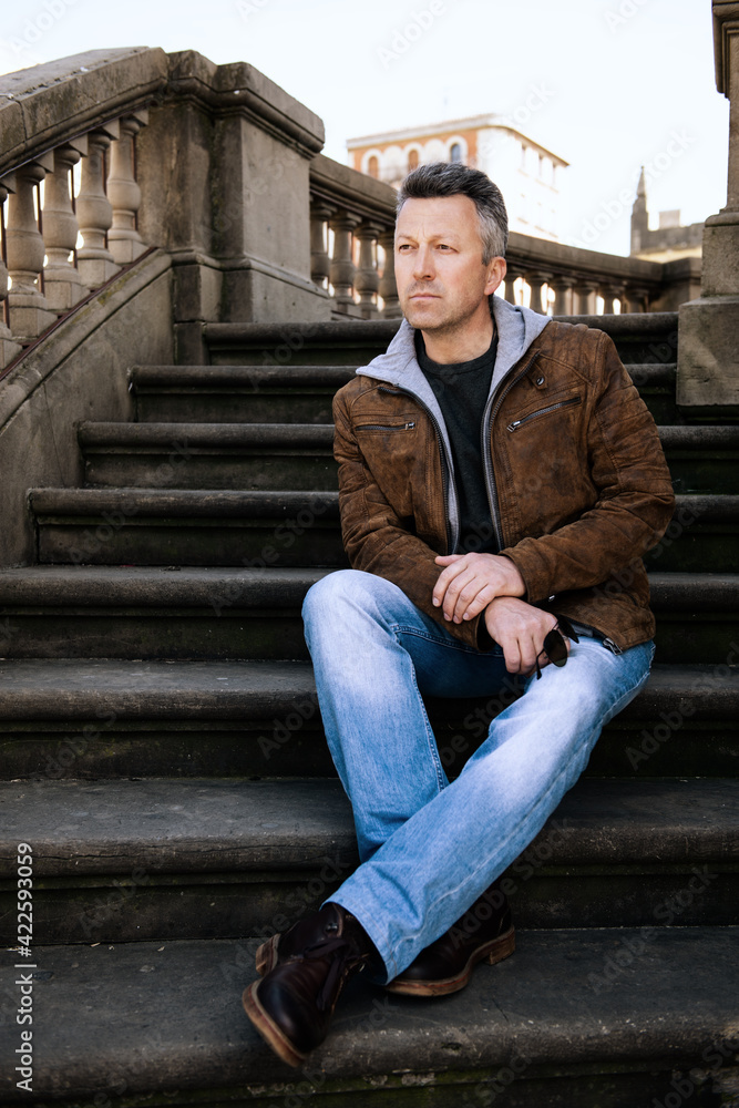 Urban outdoor portrait of a handsome man wearing blue jeans and brown jacket, street style at spring Urban outdoor portrait of a handsome man wearing blue jeans and brown jacket, street style at spring