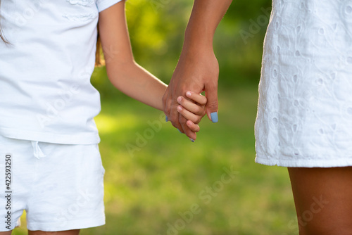 Mother leads her kid in summer forest nature outdoor. Trust, family, protection and help concept. Female and child's hands closeup against the background of summer greenery. 