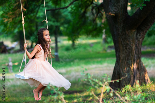 Happy girl rides on a swing in park. Little Princess has fun outdoor, summer nature outdoor. Childhood, child lifestyle, enjoyment, happiness.