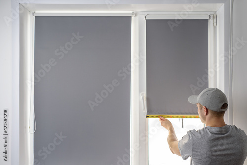 Man installing gray roller blinds on the window
