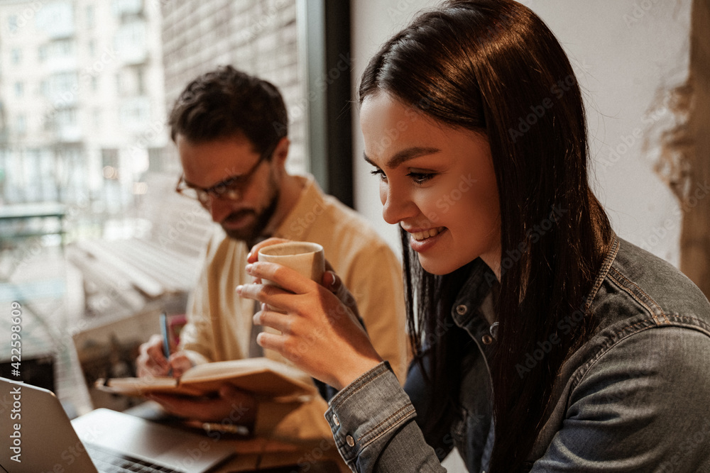 cheerful freelancer holding cup near man on blurred background