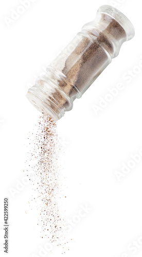 Ground black pepper spills out of a bottle for spices, flies on a white background. Isolated