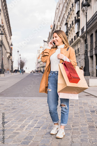 Cheerful woman is shopping in the city. She is using her smart phone.