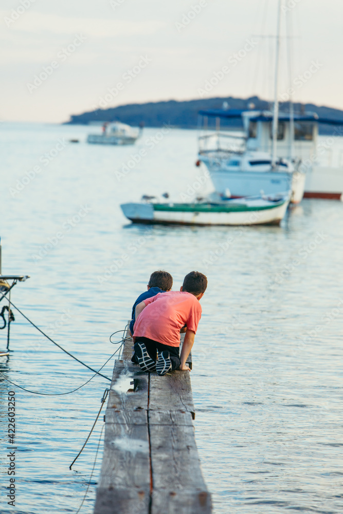 Obraz premium two little boys fishing at sea wooden pier. sea dock