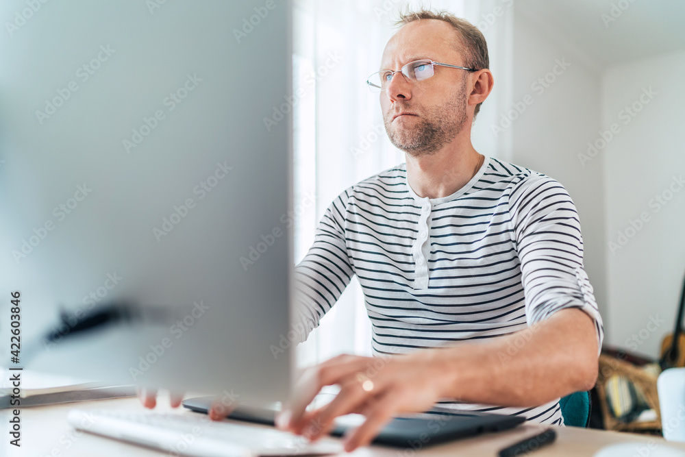 A middle-aged man in eyeglasses typing a text using a modern keyboard computer in his living room. Writing or Distance or freelance work on worldwide quarantine time concept A middle-aged man in eyeglasses typing a text using a modern keyboard computer in his living room. Writing or Distance or freelance work on worldwide quarantine time concept