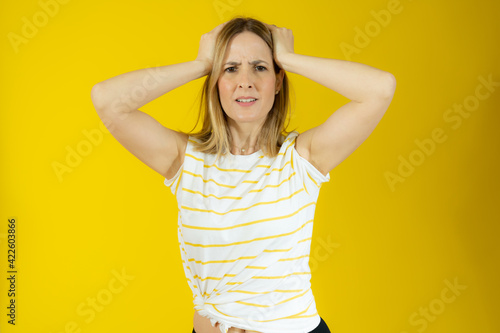 Pensive young woman in striped t-shirt isolated over yellow background