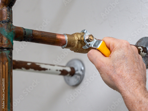 Plumber turning water shut off valve. Copper plumbing pipe with brass water supply valve and yellow stopcock handle.