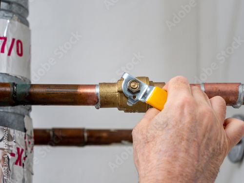 Plumber turning water shut off valve. Copper plumbing pipe with brass water supply valve and yellow stopcock handle.
