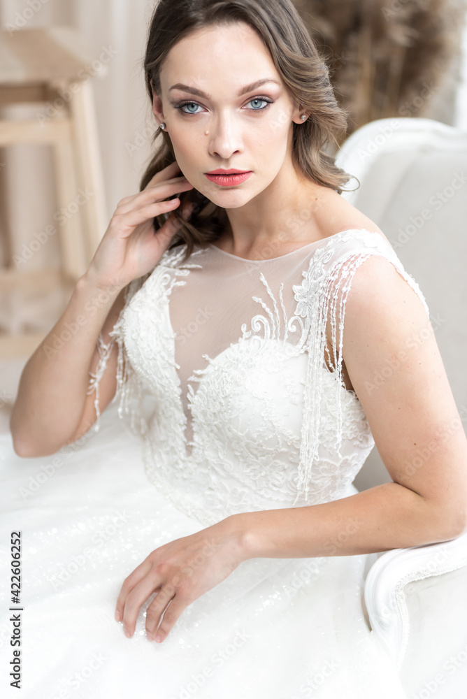 Beautiful bride in a beautiful wedding dress poses on the background of a hotel room Beautiful bride in a beautiful wedding dress poses on the background of a hotel room