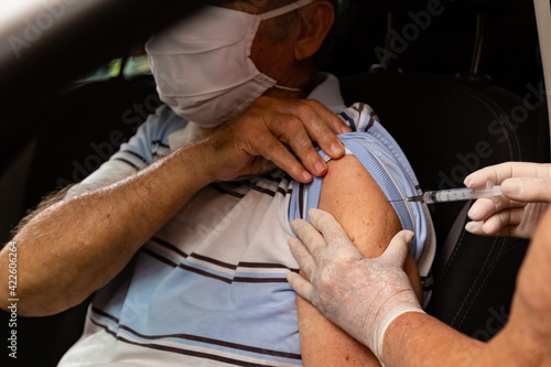 Homem idoso dentro do carro sendo vacinado por drive thru.