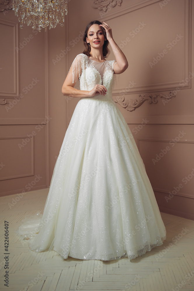 Beautiful bride in a beautiful wedding dress poses on the background of a hotel room Beautiful bride in a beautiful wedding dress poses on the background of a hotel room