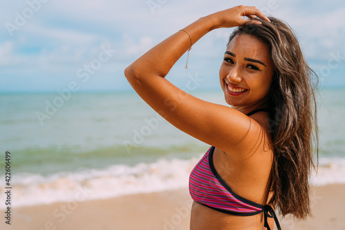 beautiful young latin american woman on the beach. woman sitting on the beach sand looking at the camera on a beautiful summer day