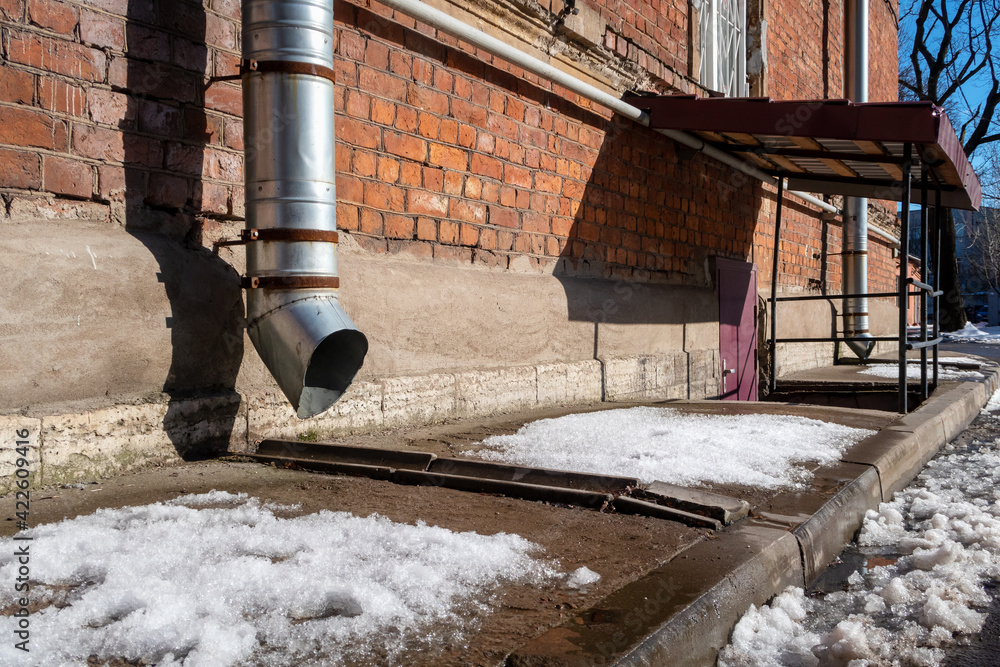 Spring melting snow on the sidewalk. Thaw in the city. The facade of an old brick house with drainpipes and an entrance to the basement. The risk of flooding of the premises due to the melting 
