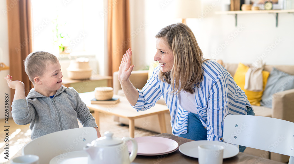 Single mother setting table for breakfast with down syndrome child at home. Single mother setting table for breakfast with down syndrome child at home.