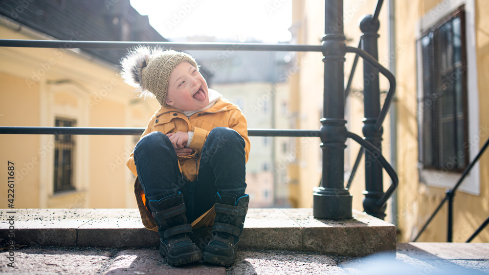 Portrait of down syndrome child outdoors in town, making faces. - obrazy, fototapety, plakaty 