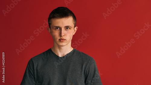 Portrait of a calm serious young guy, a student, dressed in a dark gray T-shirt standing on a red background in the studio. Transition age