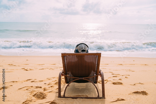 summer holidays, technology and internet concept. latin american man sitting on the beach chair, listen music with headphone and sunning on the beach © Brastock Images
