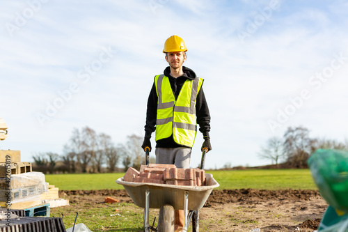 Foto A young adult male builder wearing a high visibility vest and hard hat pushing a