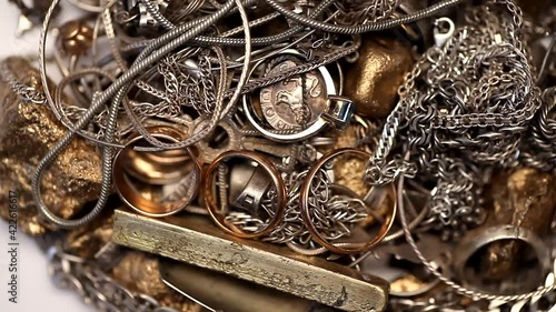 Pile of silver and gold jewelry with jewels rotating on a white background.