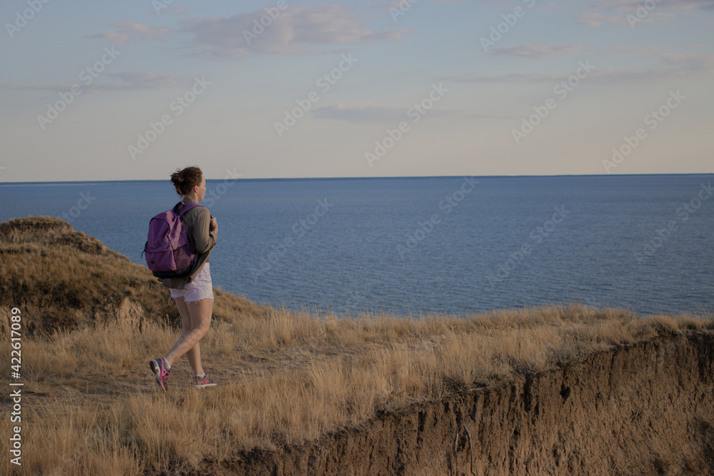 Young woman traveler with backpack walking the trail path at mountain peak, hiking to cliff by the sea during sunset,enjoying nature landscape view. Soft filter.Wanderlust adventure lifestyle concept
