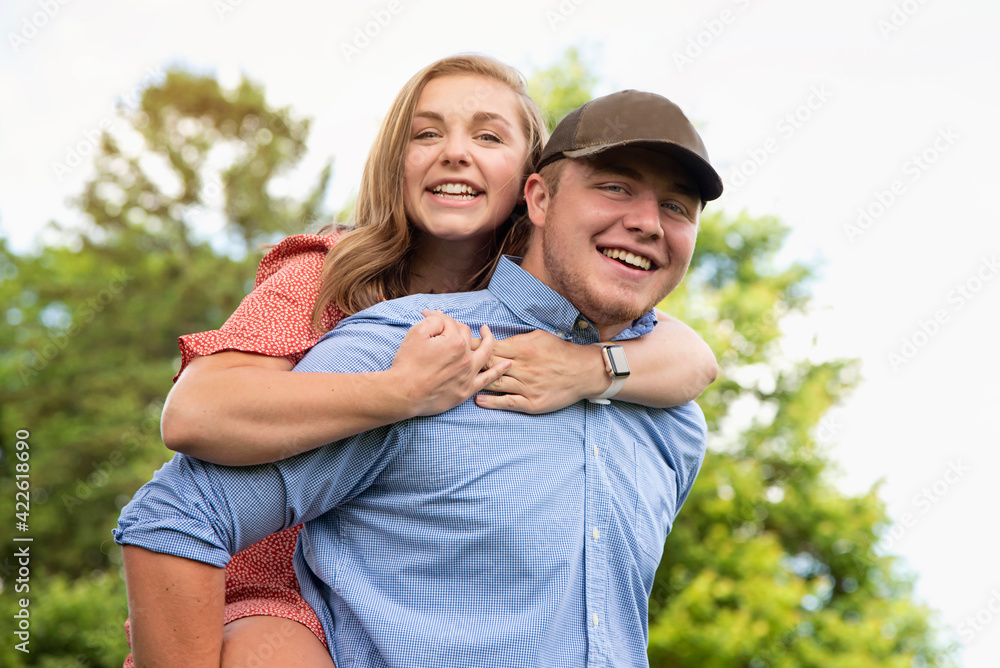 Outdoor fun spring lifestyle portrait of a young adult brother giving his young adult sister a piggyback ride