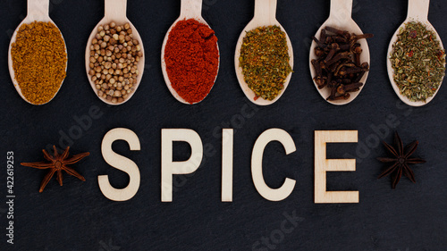 Spices in spoons and the inscription spice. Spices and herbs on a dark background