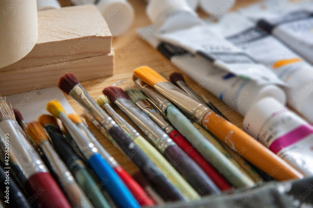 Paintbrushes, blur tempera tubes on wooden table background. Paintbrushes, blur tempera tubes on wooden table background.