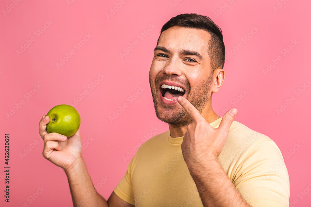 Man with perfect white teeth and green apple isolated over pink background, closeup. Showing perfect teeth and smile. Man with perfect white teeth and green apple isolated over pink background, closeup. Showing perfect teeth and smile.