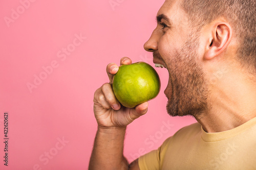 Man with perfect white teeth and green apple isolated over pink background, closeup. Showing perfect teeth and smile.