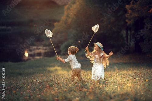 Beautiful girl and boy are catching butterflies with their butterfly net in summer park. Image with selective focus and toning