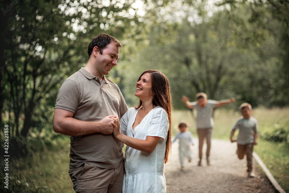 Happy married couple is hugging in the park, while their three kids are running towards them. Image with selective focus and toning. Happy married couple is hugging in the park, while their three kids are running towards them. Image with selective focus and toning.