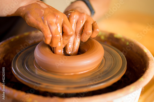 Hands of potte makes pottery dishes on potter's wheel. Sculptor in workshop makes clay product closeup