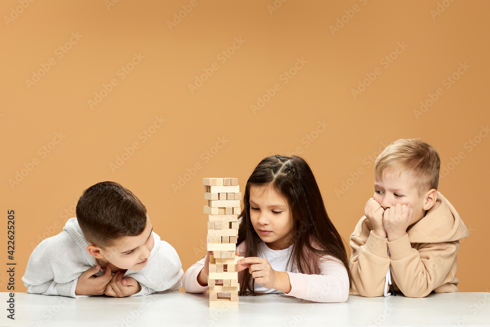 children plays with wooden constructor on desk. - obrazy, fototapety, plakaty 