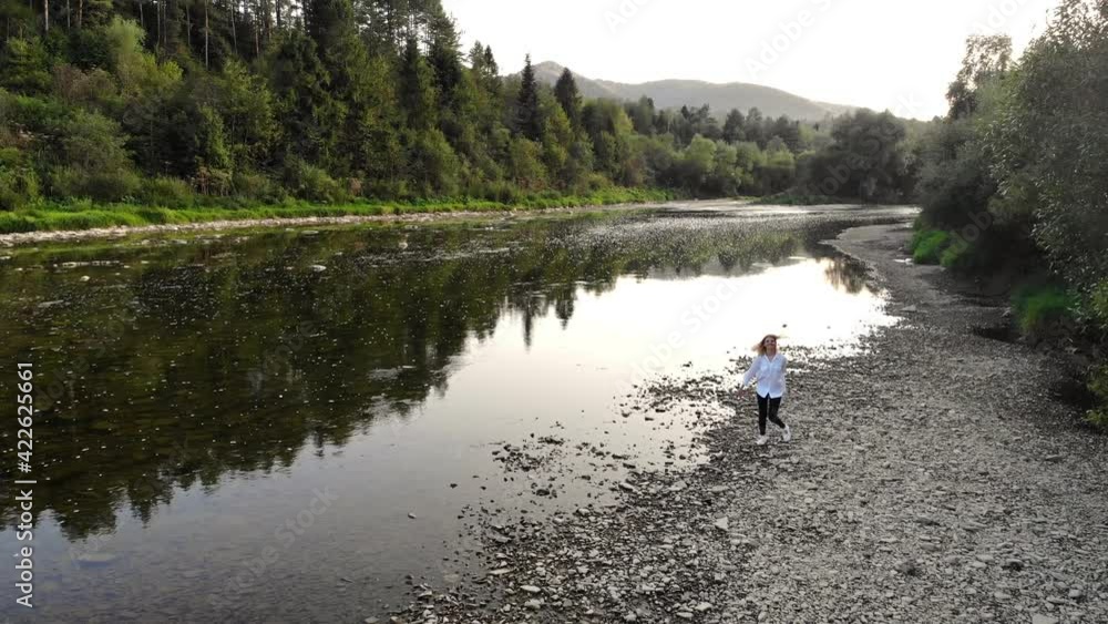 Aerial drone view of young woman in white walk along mountains river in summer morning Aerial drone view of young woman in white walk along mountains river in summer morning