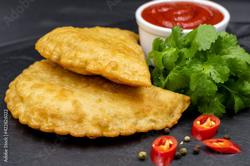 Chebureks on a black background. Served with coriander, red chili pepper and ketchup. Caucasian cuisine. photo